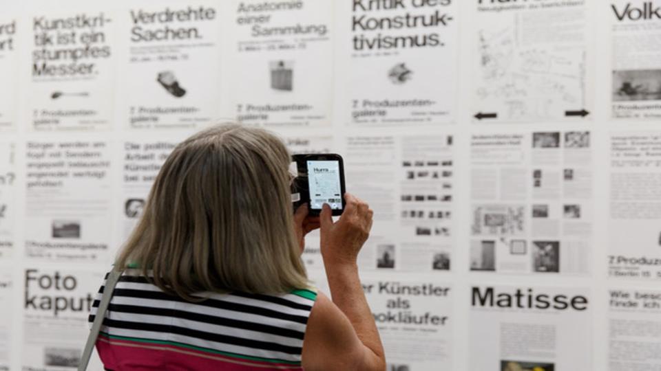 Dame fotografiert mit Mobiltelefon eine Anzeige mit Headlines
