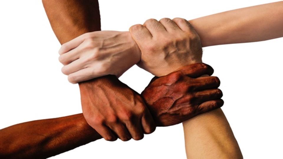 Vier ineinandergreifende Hände unterschiedlicher Hautfarben